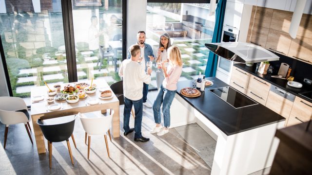 Top view of happy men and women standing in the kitchen while holding wine and eating pizza