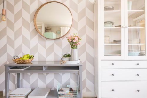 Mirror on patterned wallpaper above grey table with flowers in scandi living room interior
