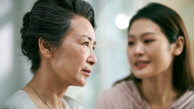 asian adult daughter talking to and comforting senior mother who is living with mental illness