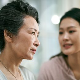 asian adult daughter talking to and comforting senior mother who is living with mental illness
