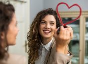 Smiling businesswoman is drawing heart with lipstick on the mirror while preparing for work.