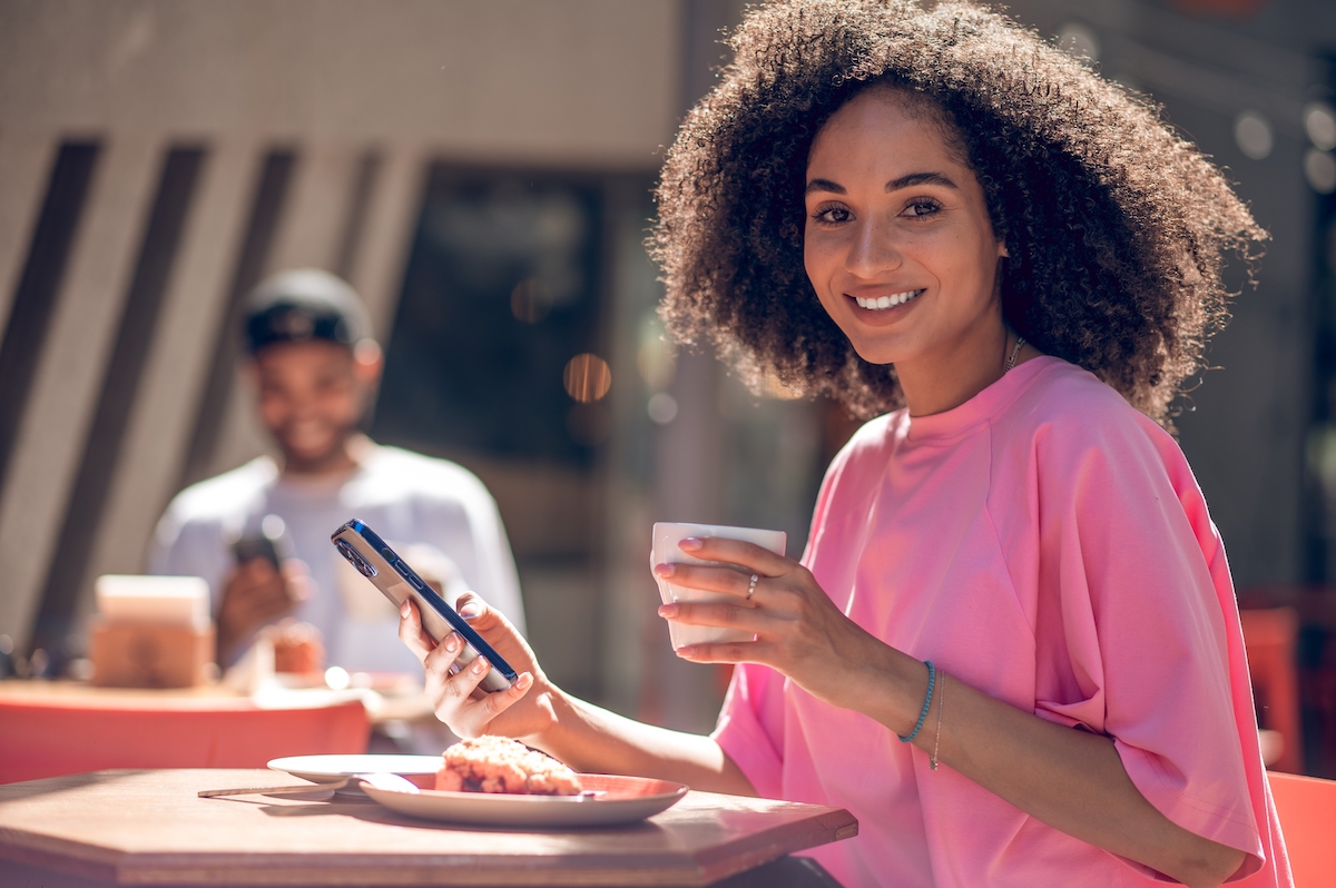 Cute curly-haired young woman in pink shirt in a street cafe with a man in the background