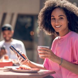 Cute curly-haired young woman in pink shirt in a street cafe with a man in the background