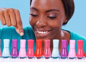 Close up of a young smiling woman leaning over a row of nail polish in different colors