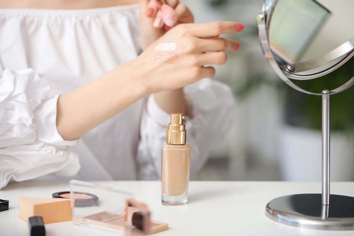 Woman testing foundation on her hand, sitting in front of a mirror.