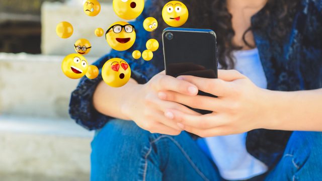 Close-up of woman using smartphone sending emojis.
