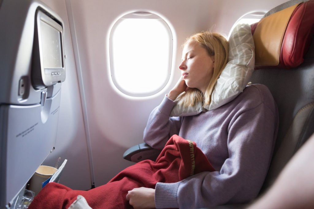 Young woman wearing neck pillow sleeping in window seat of plane