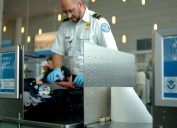 TSA agent scanning luggage through X-ray security checkpoint machine.