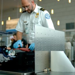 TSA agent scanning luggage through X-ray security checkpoint machine.