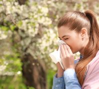 Sneezing young girl with nose wiper among blooming trees in park