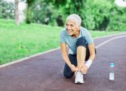 Portrait of a happy active beautiful senior woman posing fixing shoelace on her running shoe after exercising outdoors