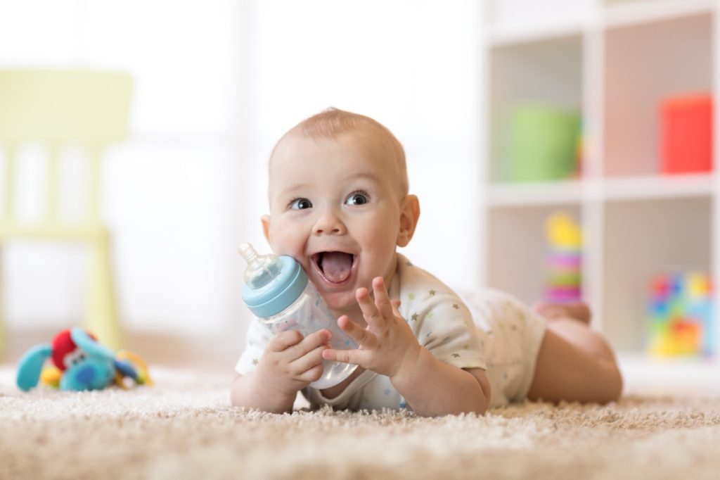 A baby crawling on the carpet with a bottle