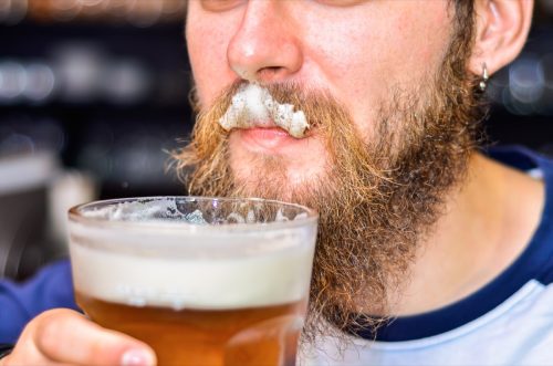 bearded man drinking beer and foam on mustache