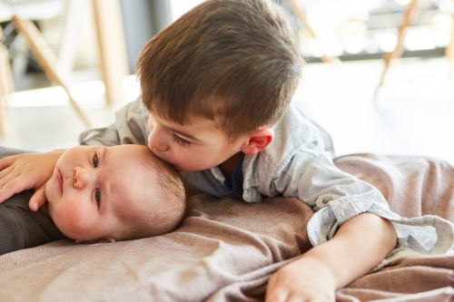 Little boy as big brother gives baby a kiss on the forehead