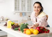 Thực phẩm lành mạnh để tăng cường hệ thống miễn dịch của bạn.  Người phụ nữ trẻ tươi cười xinh đẹp nấu món salad hữu cơ tươi tại nhà trong căn bếp hiện đại, nhặt rau