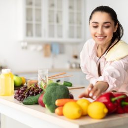 Healthy Food To Boost Your Immune System. Beautiful smiling young woman cooking fresh organic salad at home in modern kitchen, reaching for vegetables