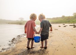 two little boys carrying a bucket on the beach