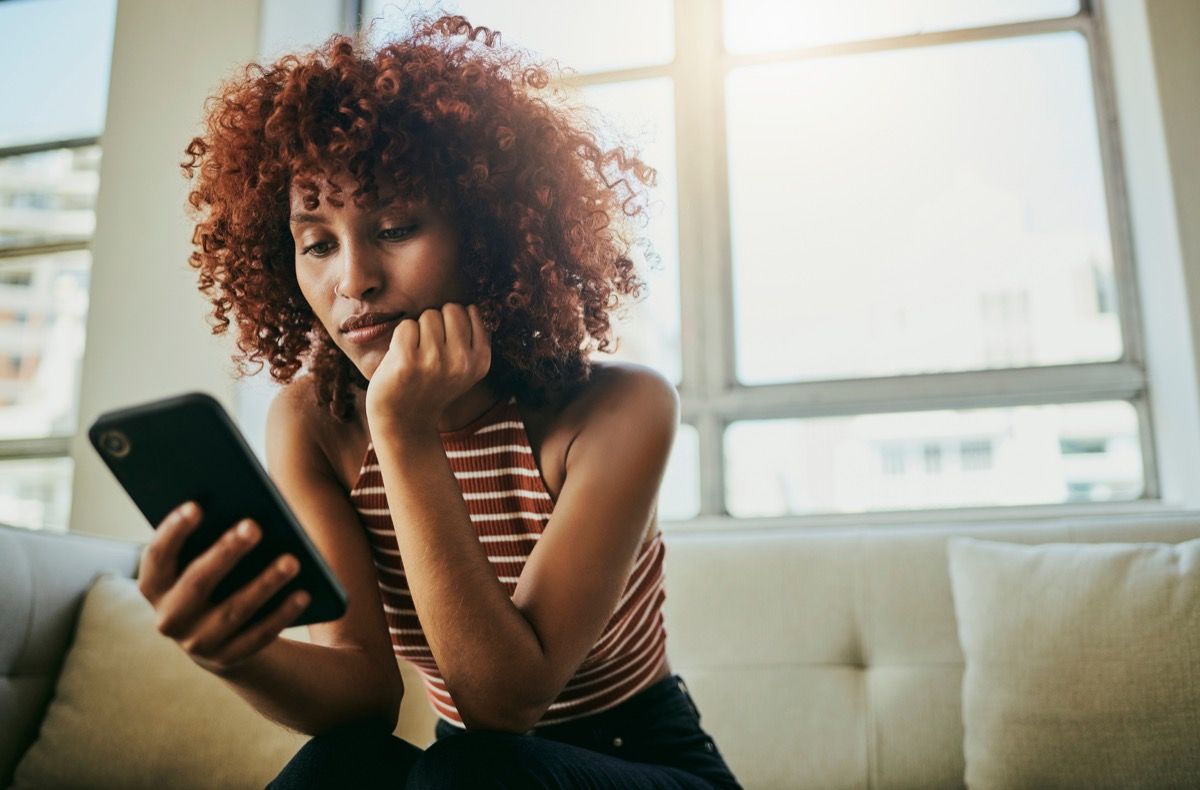 Woman sitting on sofa and scrolling through phone looking bored