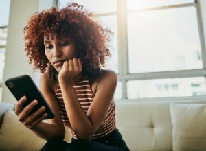 Woman, phone and home sofa while online for communication on social media mobile app chat. Bored person with smartphone typing email, blog post or search on internet waiting on slow wifi connection