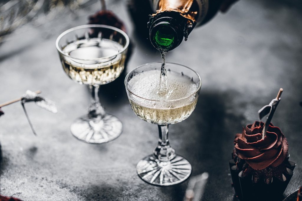 Close-up of pouring champagne in a glasses over black table with cup cake. Serving drinks for new years party.