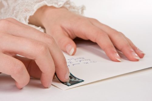 Female hands sticking a stamp on an envelope (the address is the most common one in the US)i