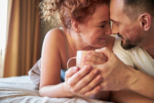 Cropped photo of smiling lovely couple with coffee lying in bed