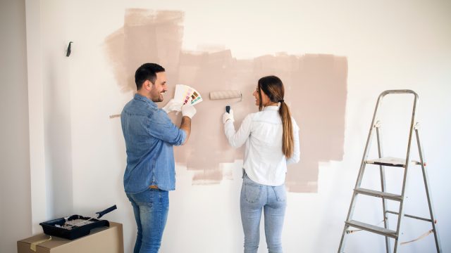 Couple renovating their apartment while man holding color palette and woman painting walls with roller.