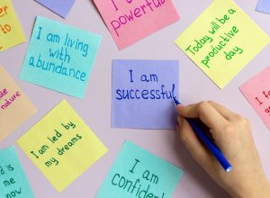 Close up of a hand writing positive affirmations on colorful Post-it notes.