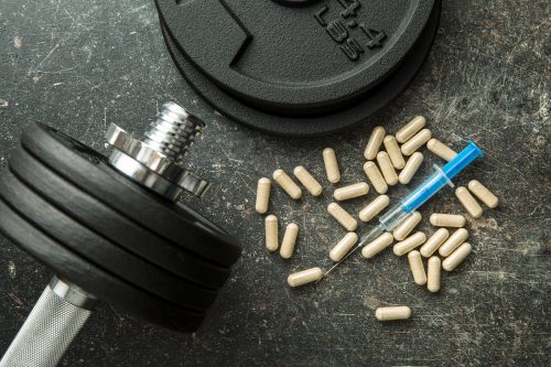 Syringe and pills next to weights