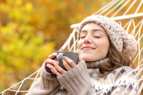Relaxed woman smelling coffee lying on hammock in autumn holidays