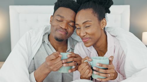 man and woman smiling as they drink coffee in bed