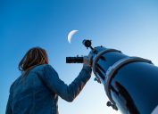Một phụ nữ trẻ nhìn mặt trăng khi đứng cạnh kính thiên văn
