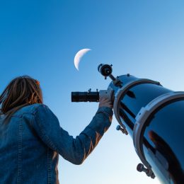 A young woman looking up at the moon while standing next to a telescope