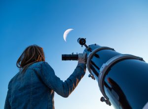 A young woman looking up at the moon while standing next to a telescope