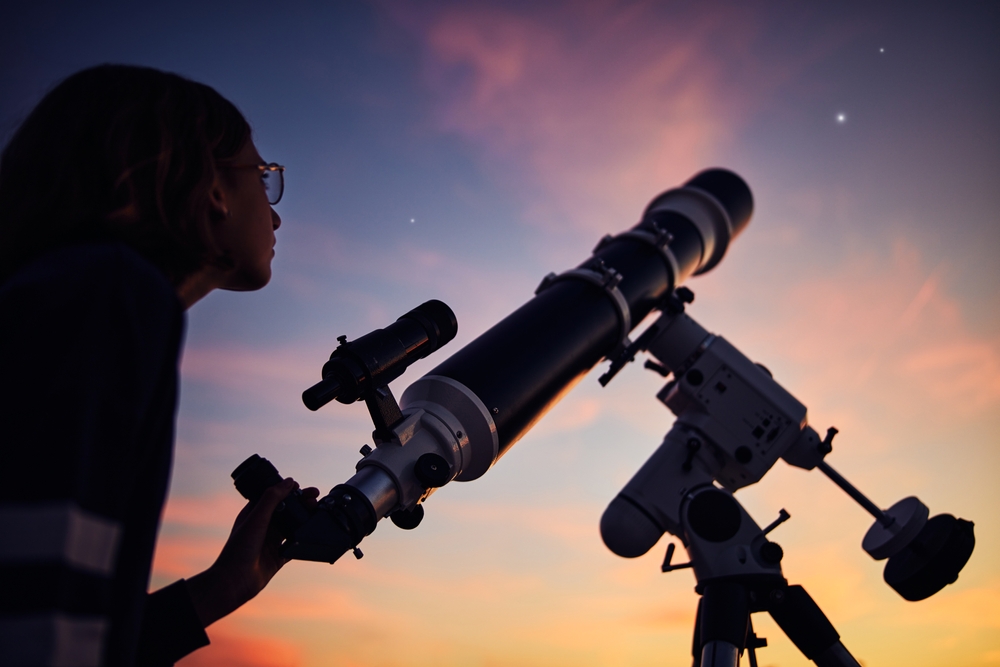 A young girl looking at the night sky with a telescope