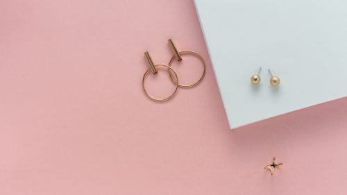 Golden stud earrings and ring on white and pink paper background with copy space