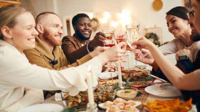 Multi-ethnic group of people raising glasses sitting at beautiful dinner table celebrating Christmas with friends and family, copy space