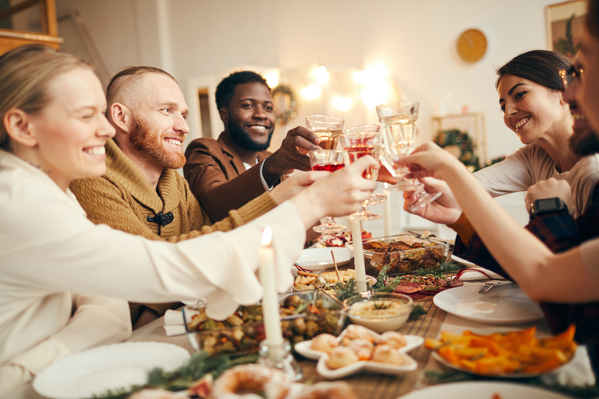 Nhóm người đa sắc tộc nâng ly ngồi bên bàn ăn tối tuyệt đẹp mừng Giáng sinh cùng bạn bè và gia đình, sao chép không gian