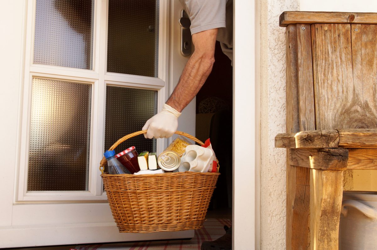 hand of man is taking a full willow wicker basket with handle at he front door. home delivering some groceries at quarantine time because of coronavirus infection COVID-19