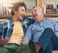 man sitting on the couch sharing funny knock-knock jokes with his father