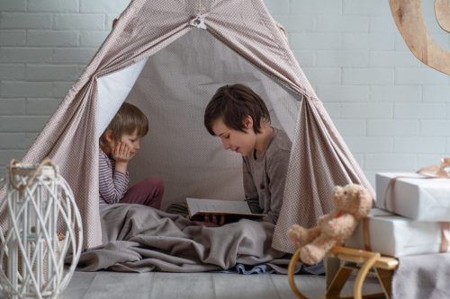 big brother reading to his little brother in a homemade fort