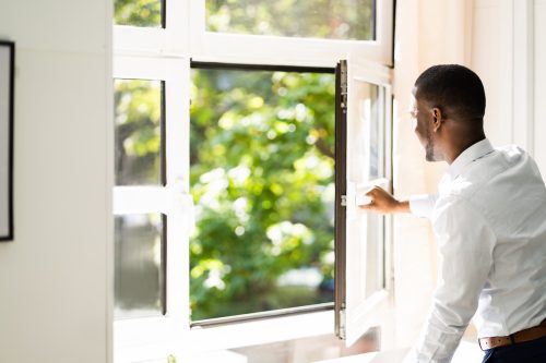 Side view of a man in a white button-down shirt opening a window on a sunny day