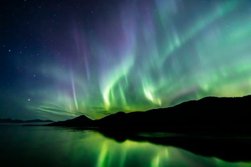 The Northern Lights in the sky above hills on a coastline