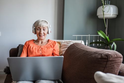 Người phụ nữ cao cấp hạnh phúc nằm trên ghế sofa và nhìn vào máy tính xách tay