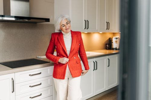 Happy senior woman trying on a new jacket in front of the mirror. Mature woman smiling and admiring her reflection while wearing a beautiful red jacket.