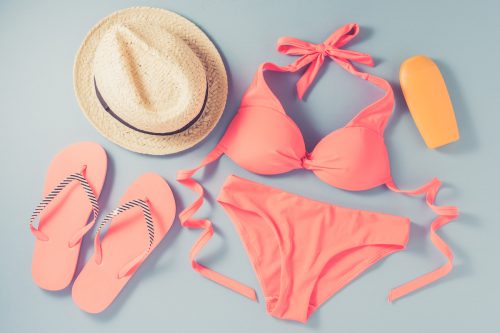 Coral-colored bikini and flip flops with a sun hat on a gray background
