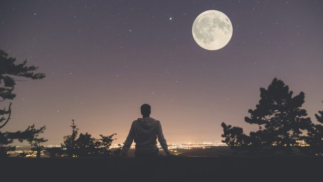 A person looking at a full moon over a city