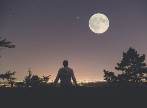 A person looking at a full moon over a city