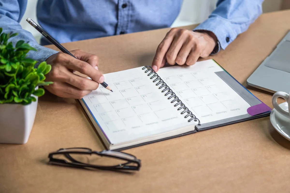 Close up of a person writing in a planner on a desk