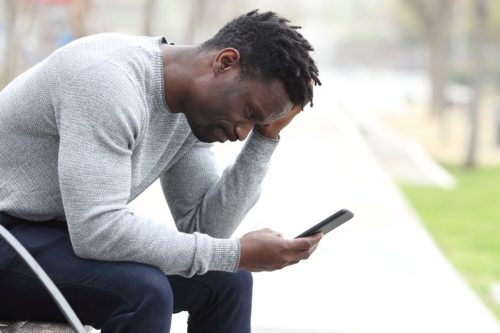 man looking upset while reading through text messages